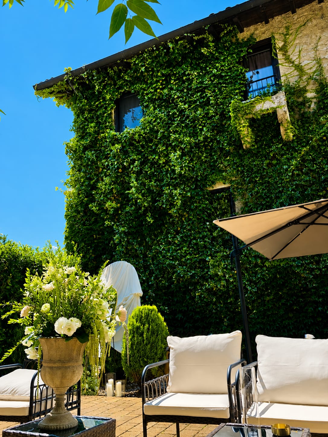 Stone facade of Villa Sant'Erasmo covered in ivy, with a garden seating area