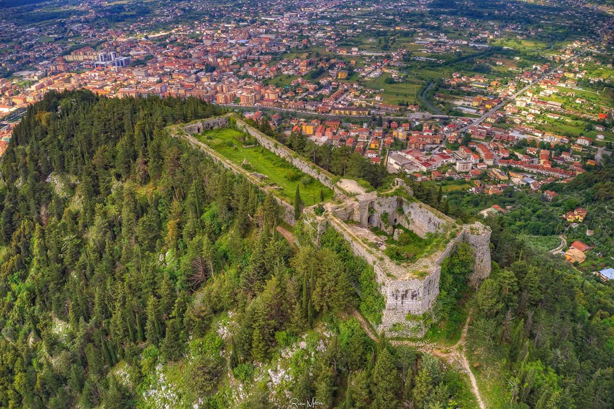 The ruins of Sora Castle atop a wooded hill, with the red-roofed town in the valley below