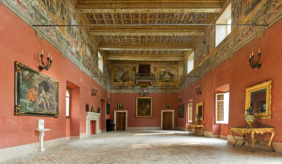Interior hall of Castello Boncompagni in Isola del Liri with terracotta-coloured walls, a gilded and blue coffered ceiling, a frescoed frieze, a rococo console and a mosaic floor