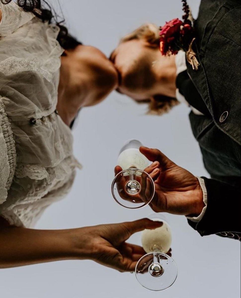 The newlyweds kiss and toast with glasses against the sky