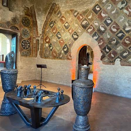 Interior hall of the Palace of Boniface VIII in Anagni with medieval frescoes of diamonds and medallions, a warmly lit pointed arch and a terracotta floor