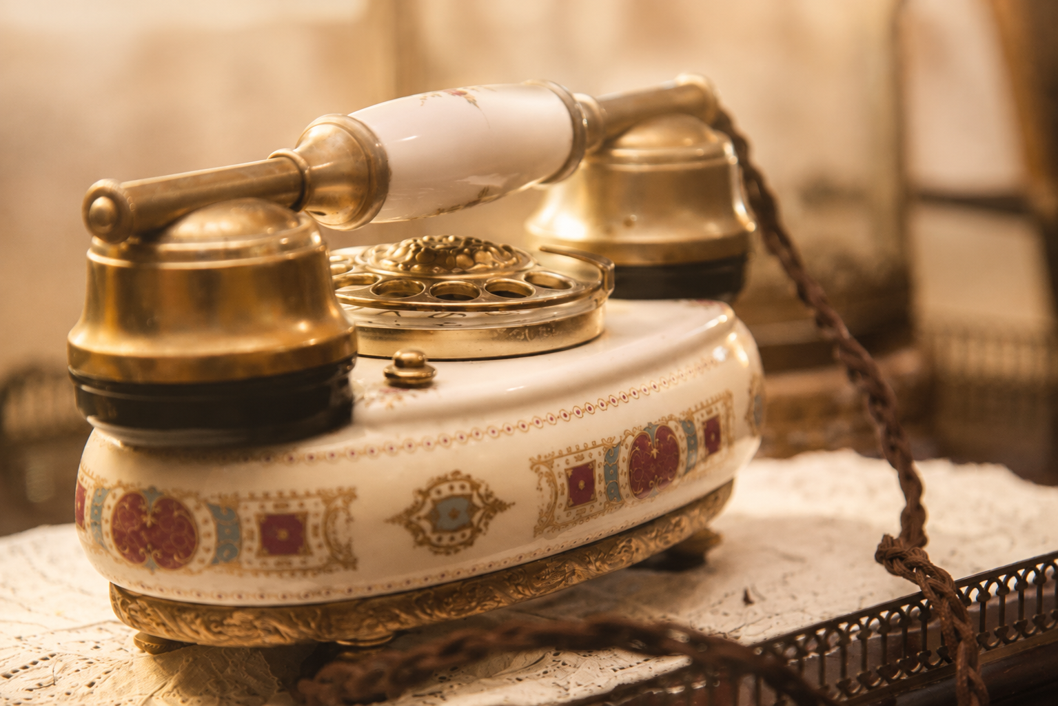 Antique porcelain and brass telephone on an embroidered table