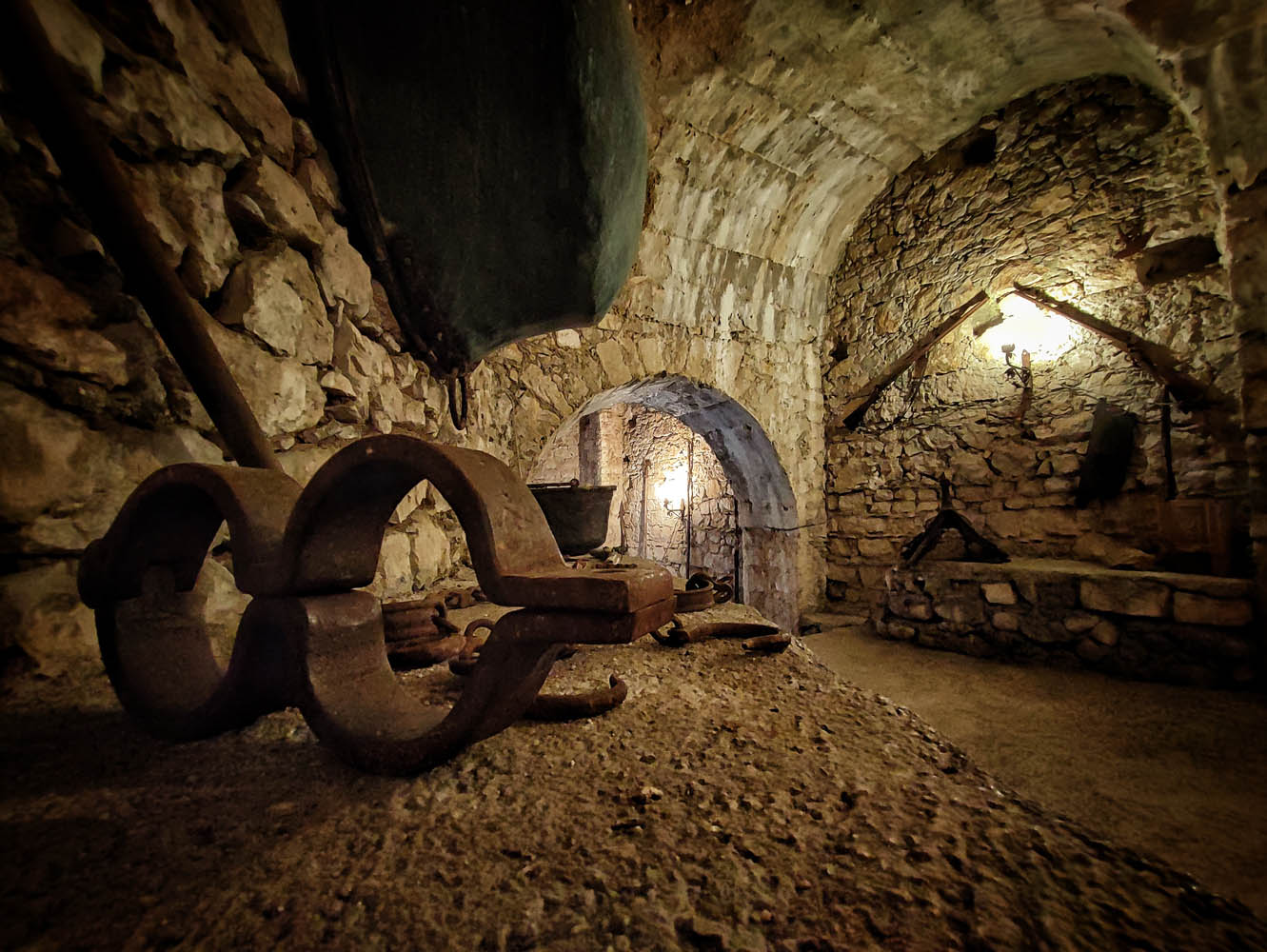 Stone underground chambers of Fumone Castle with old stocks and instruments lit by warm light