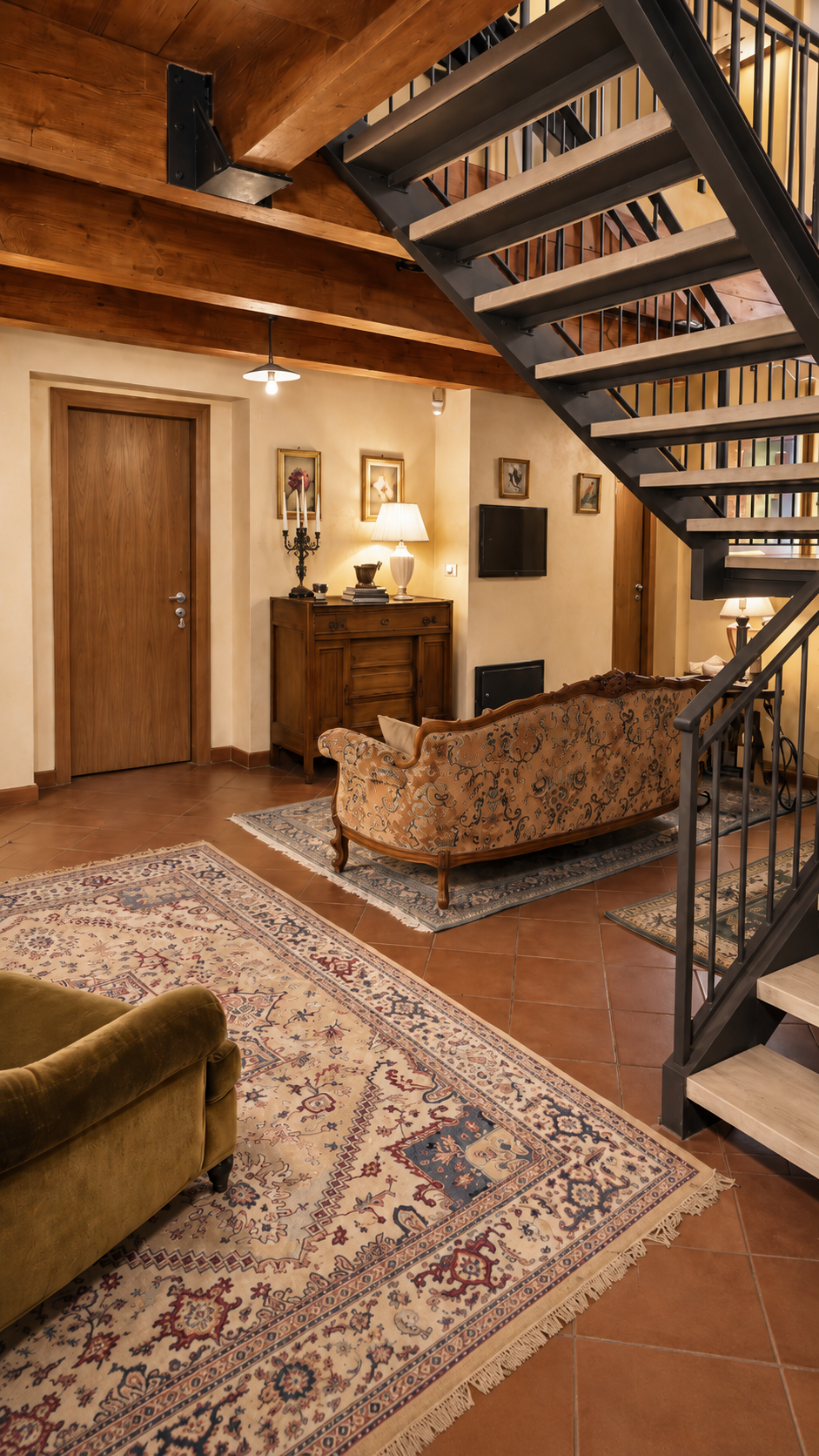 Sitting room beneath the iron and wood staircase at Villa Sant'Erasmo, with a period sofa and rugs