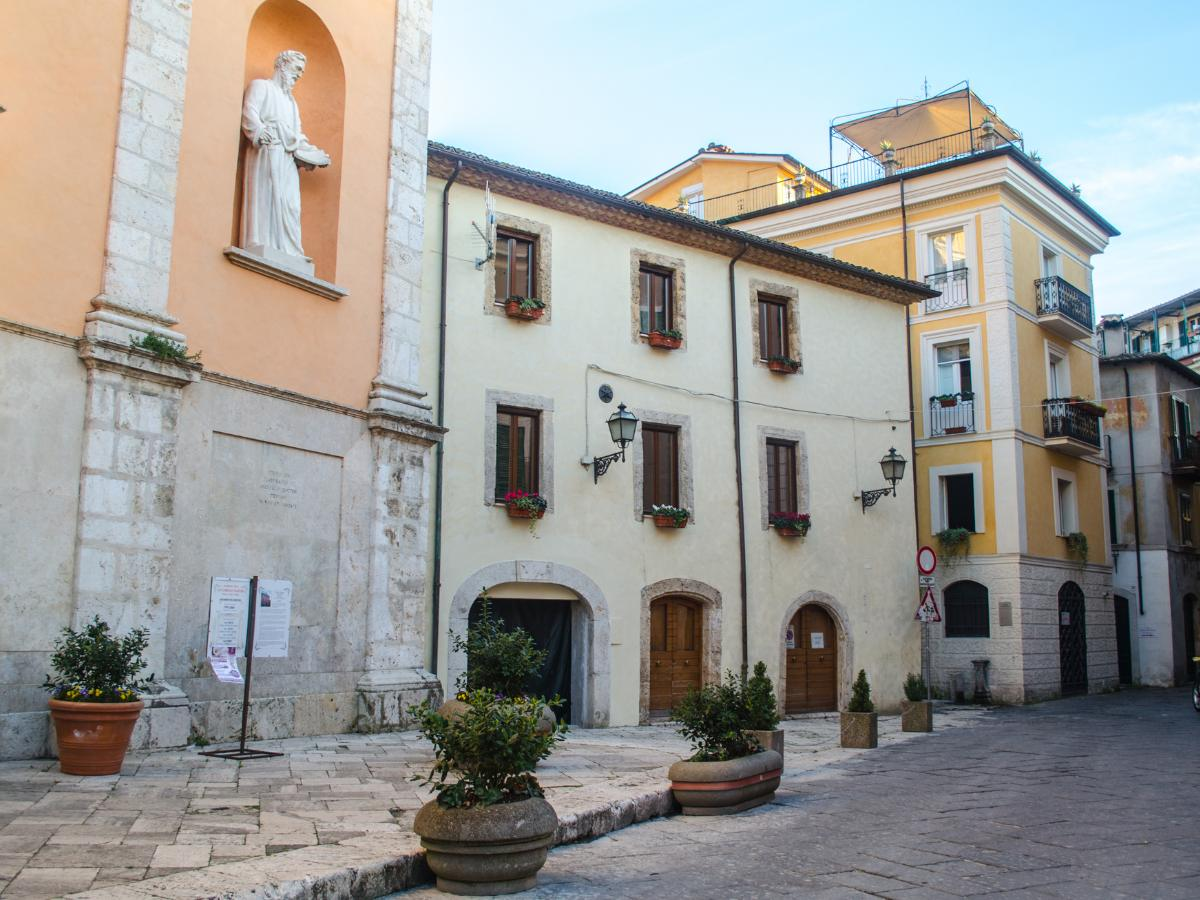 Square in the old town of Isola del Liri with cream and yellow buildings, niche statues, stone arches and flower pots