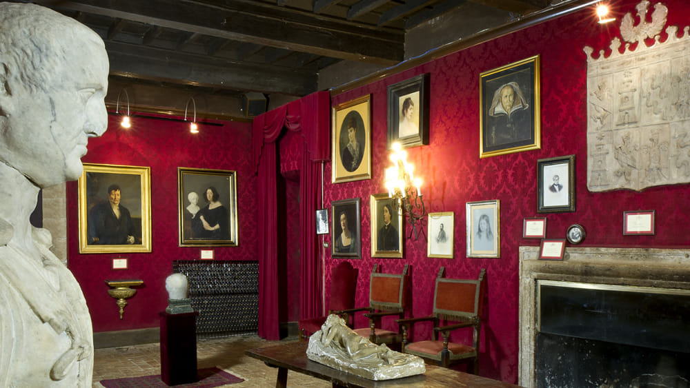 Interior hall of Fumone Castle with red damask walls, antique paintings and a stone fireplace