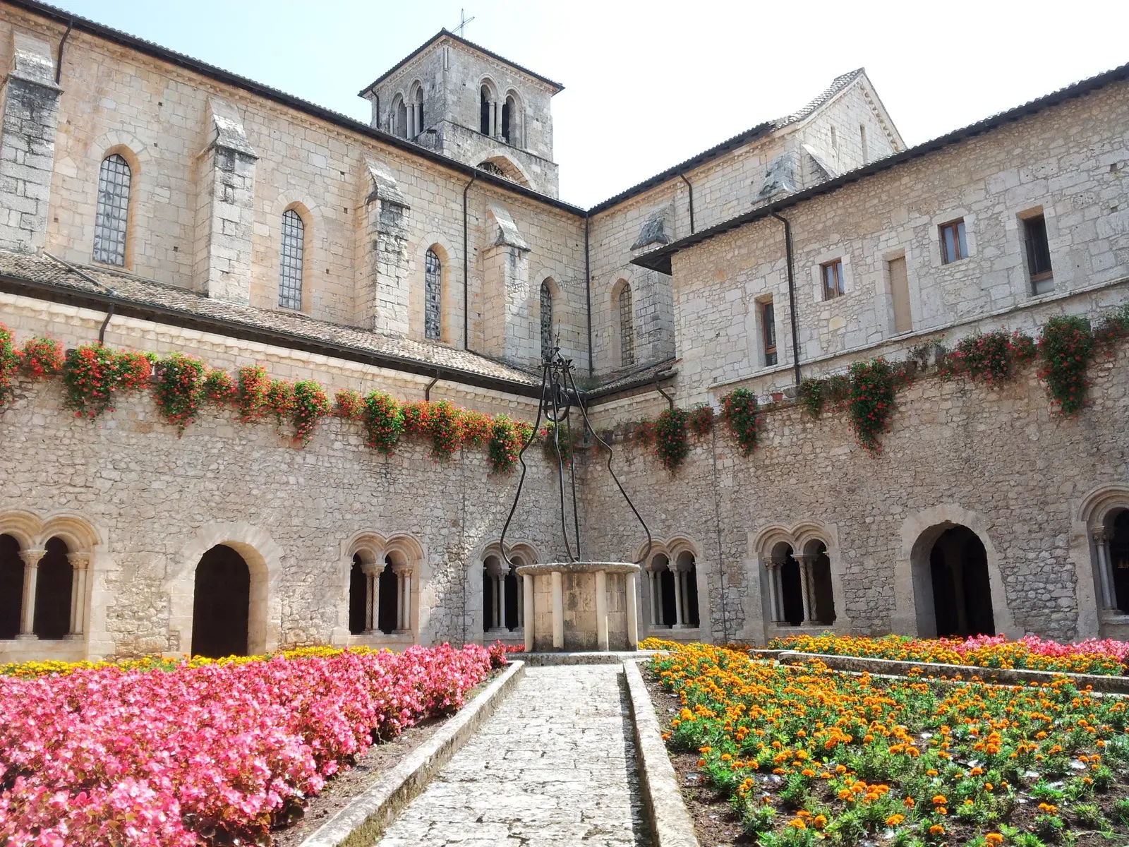 The cloister of Casamari Abbey with a stone well at its centre, arcades of paired columns and flowerbeds of roses along the path