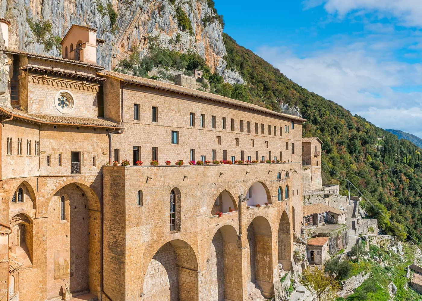 The Sacro Speco of Subiaco clinging to the rock face, with its terrace of red flowers and the green forest of the Aniene valley