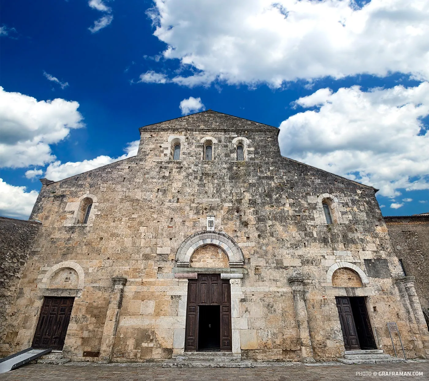 The Romanesque facade of Anagni Cathedral in limestone, with three portals and a rose window under a blue sky